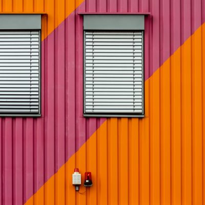 A background of an orange and purple metal wall with white window blinders